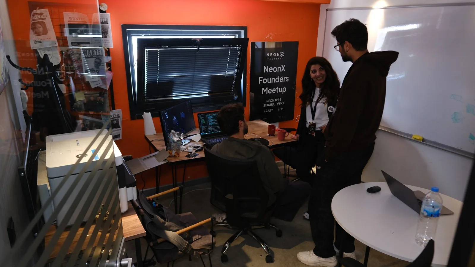 Colleagues talking beside a NeonX Founders Meetup poster in the Istanbul office