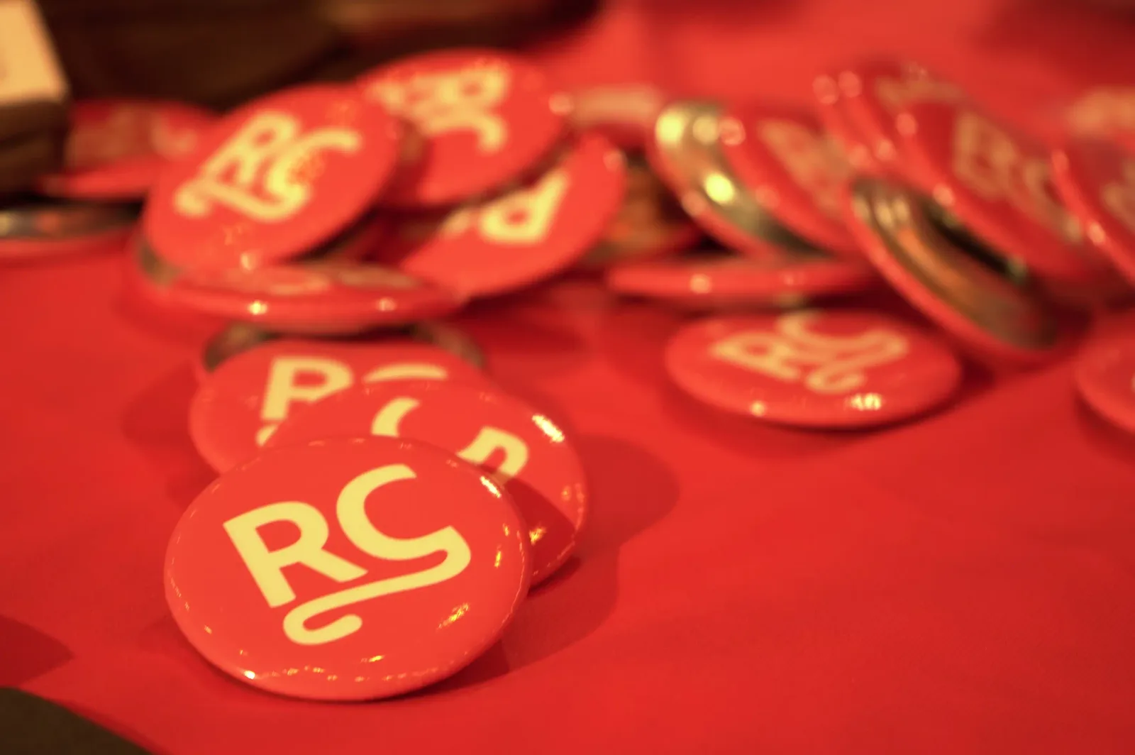 RevenueCat RC branded pin badges and promotional items on a red tablecloth showcasing the Neon Apps x RevenueCat partnership