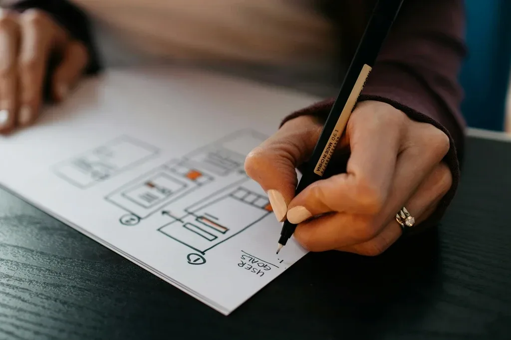 Person sketching website wireframe on paper during UX design planning