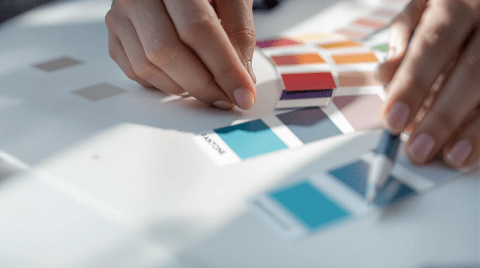 Designer hands arranging Pantone colour chips in deliberate branding groupings