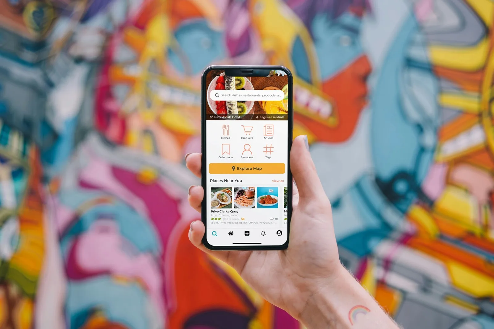 Hand holding a phone showing a food discovery app in front of a graffiti wall