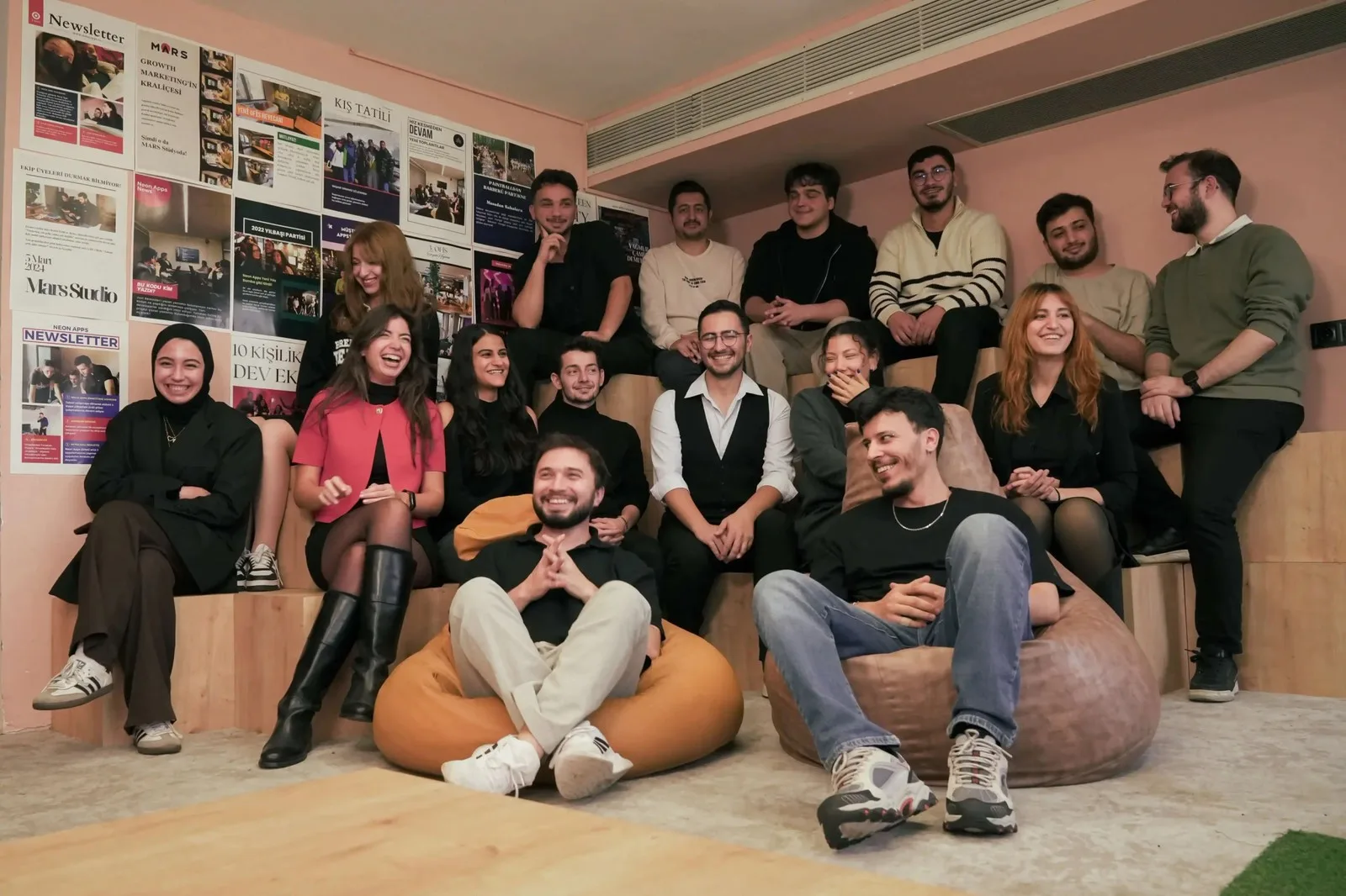 The Neon Apps team sitting together on tiered seating in front of a wall of newsletters