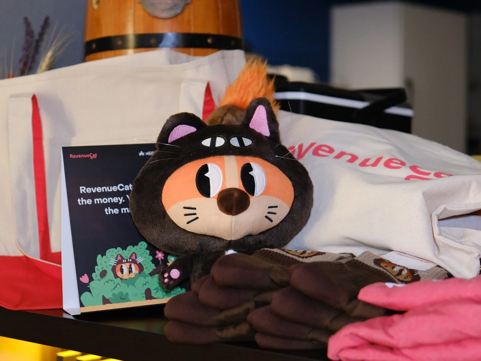 RevenueCat plush mascot with a tote bag, socks and a card on a table