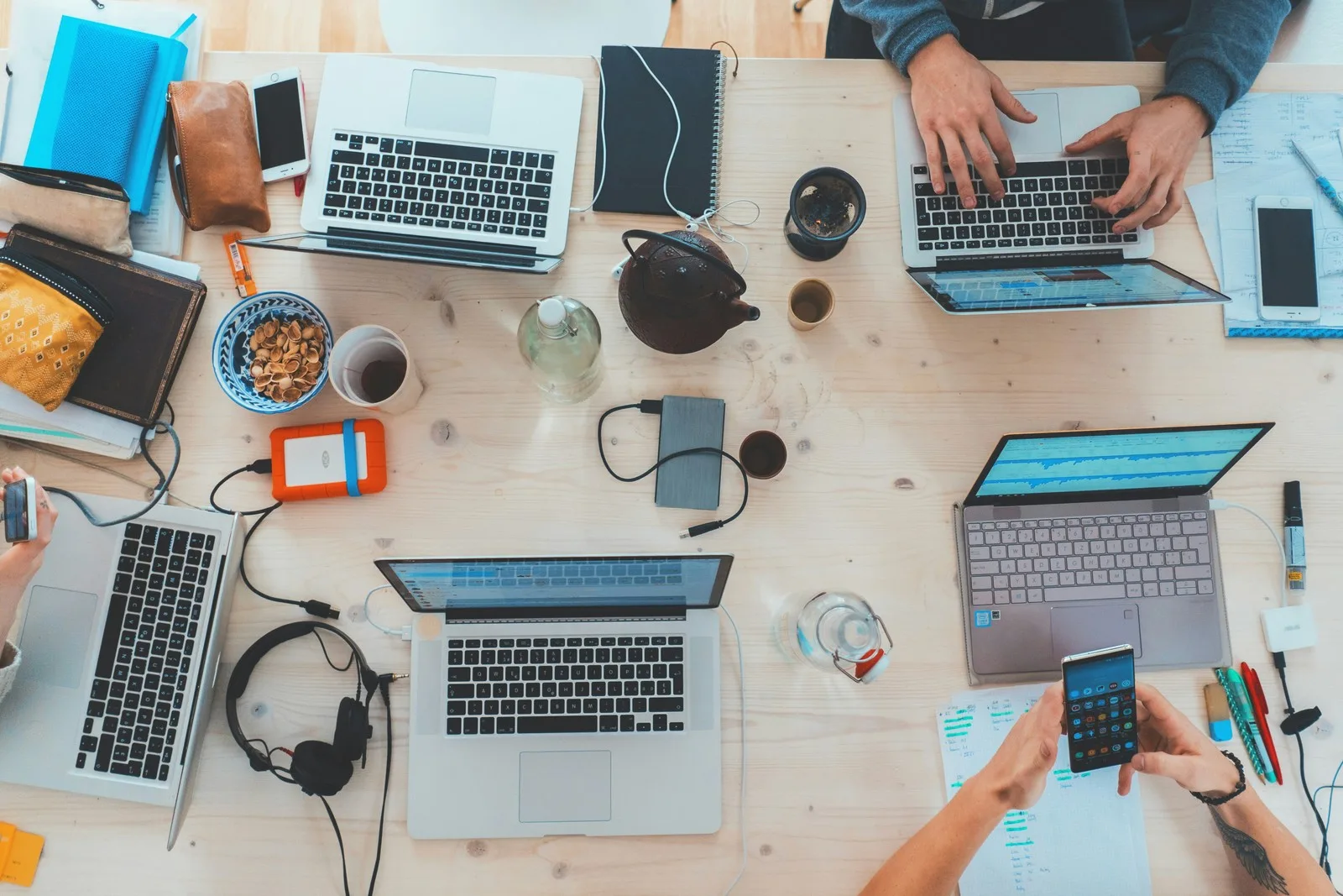Collaborative workspace with laptops, smartphones, external storage devices, and productivity tools for digital product development.