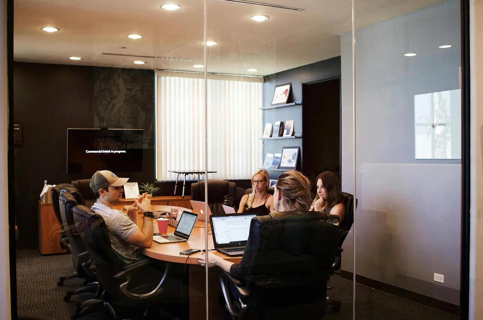 Four colleagues with laptops in a glass walled meeting room
